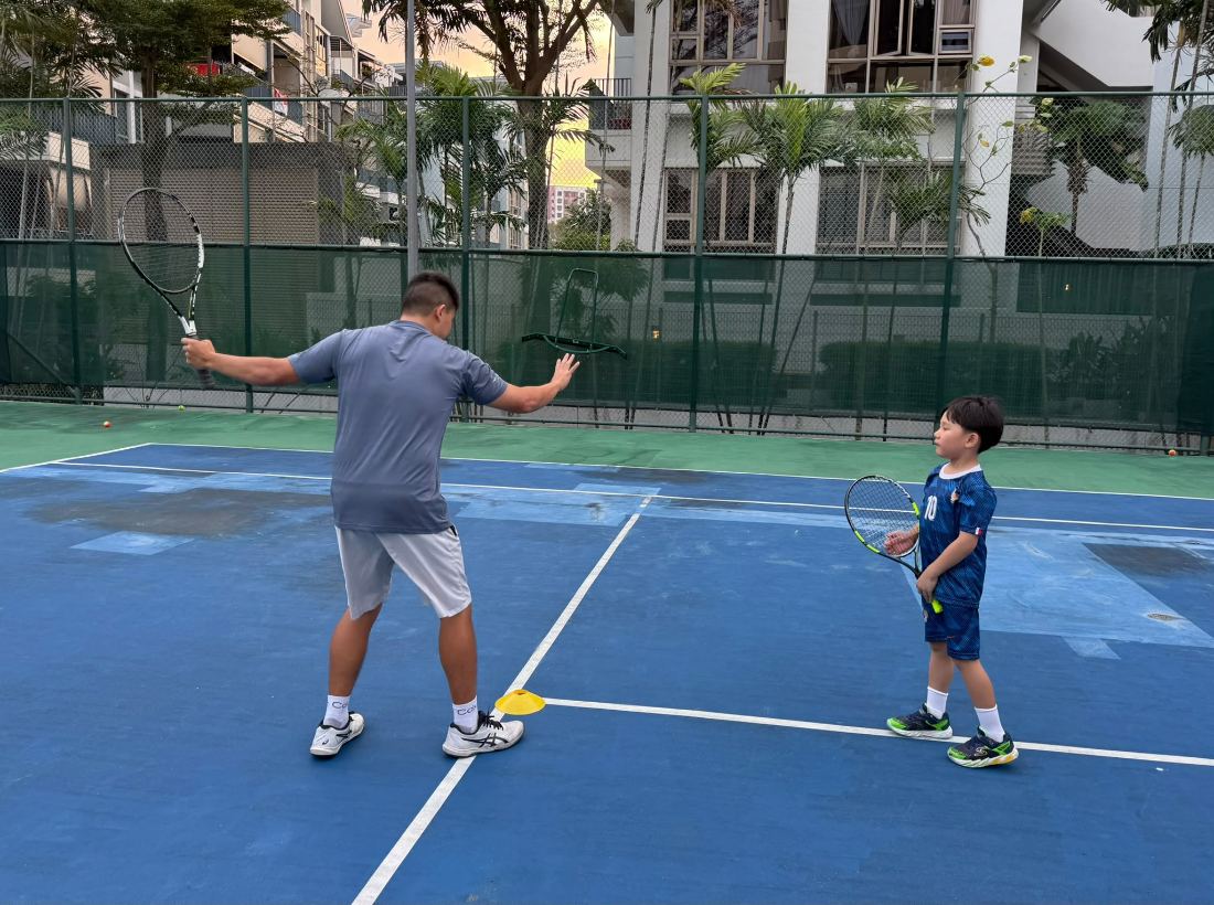 Sherwin Foo demonstrating a forehand beside a young player
