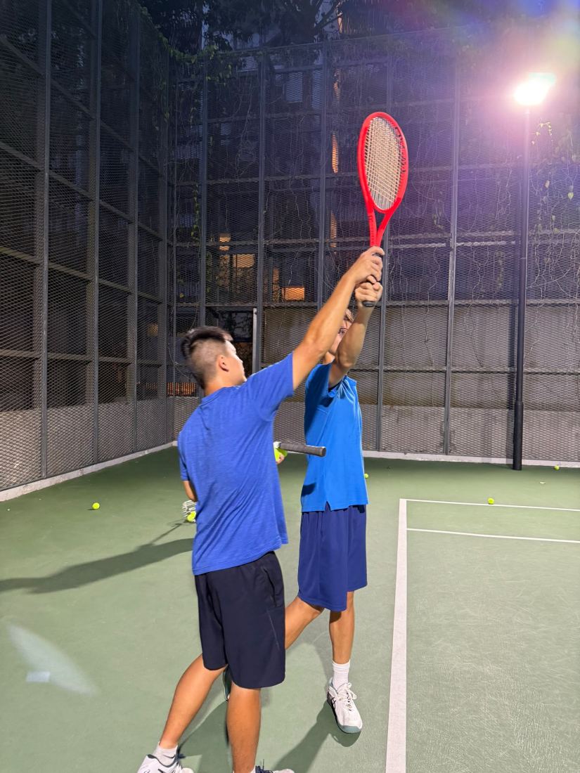 Sherwin Foo guiding a junior through the overhead reach on the serve